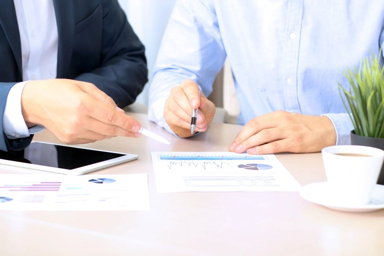 Two people sitting at a table with papers and pens.